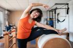 Fotografia de uma senhora se esticando em barril no estúdio de pilates.